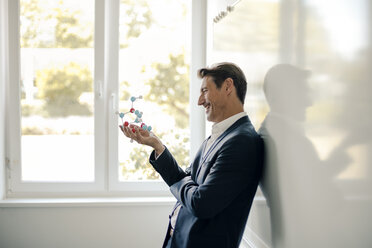 Successful businessman leaning on whiteboard, holding molecule model - GUSF01061