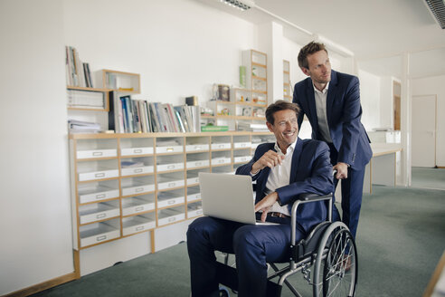 Colleague pushing businessman, sitting in wheelchai´r - GUSF01087