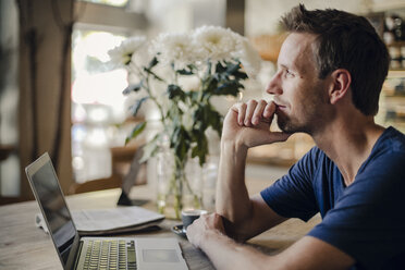 Mid adult man sitting in coffee shop, using laptop - GUSF01093