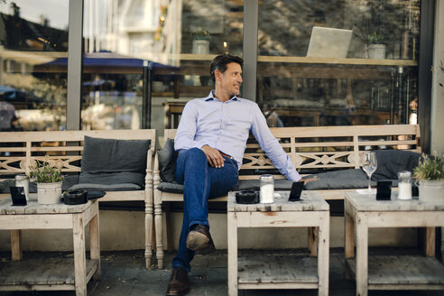 Businessman sitting in coffee shop, smiling - GUSF01096