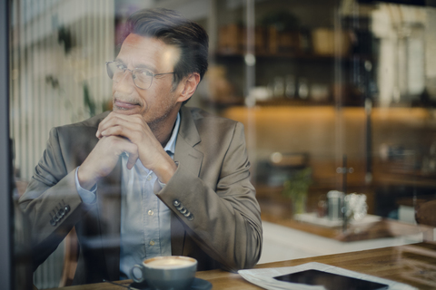 Älterer Geschäftsmann sitzt in einem Café und lächelt, lizenzfreies Stockfoto