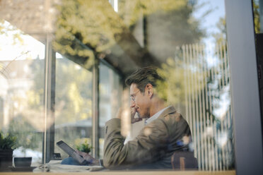 Mature businessman sitting in coffee shop, using digital tablet - GUSF01115