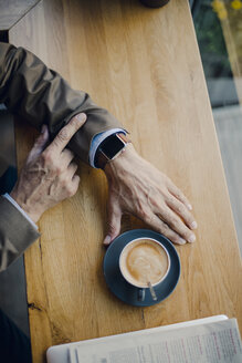 Mature businessman sitting in coffee shop, checking time - GUSF01116