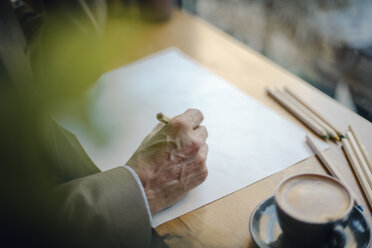 Älterer Geschäftsmann sitzt in einem Café und zeichnet auf Papier - GUSF01118