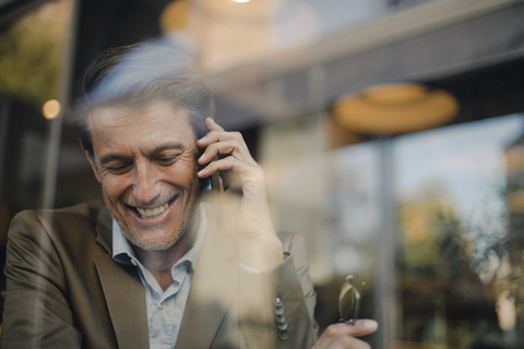 Älterer Geschäftsmann sitzt in einem Café und spricht am Telefon, lizenzfreies Stockfoto