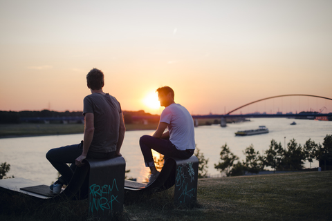 Zwei Freunde beobachten den Sonnenuntergang am Fluss, lizenzfreies Stockfoto
