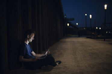 Mittlerer erwachsener Mann im Schneidersitz auf dem Boden sitzend, der nachts einen Laptop benutzt - GUSF01125