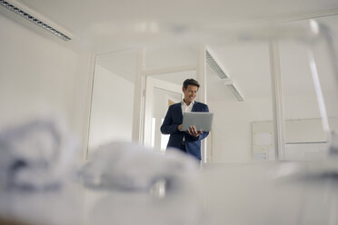 Businessman standing in office, using laptop - GUSF01142