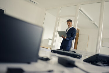 Businessman standing in office, using laptop - GUSF01143