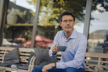 Mature businessman sitting in coffee shop, drinking coffee - GUSF01155