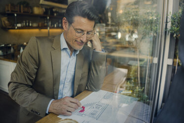 Mature businessman sitting in coffee shop, drawing outline of a house - GUSF01160