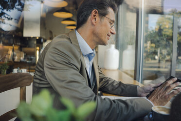 Älterer Geschäftsmann, der in einem Café sitzt und ein digitales Tablet benutzt - GUSF01167