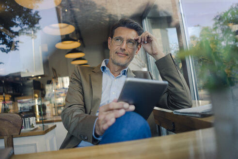 Älterer Geschäftsmann, der in einem Café sitzt und ein digitales Tablet benutzt - GUSF01168