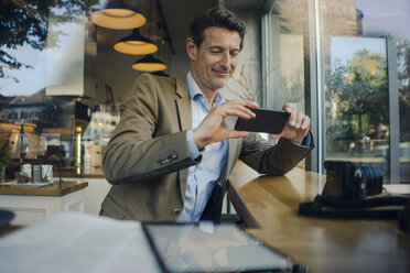 Mature businessman sitting in coffee shop, using smartphone - GUSF01173