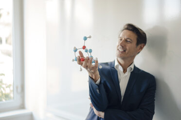 Successful businessman leaning on whiteboard, holding molecule model - GUSF01180