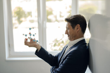 Successful businessman leaning on whiteboard, holding molecule model - GUSF01181