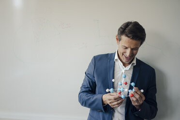 Successful businessman leaning on whiteboard, holding molecule model - GUSF01182