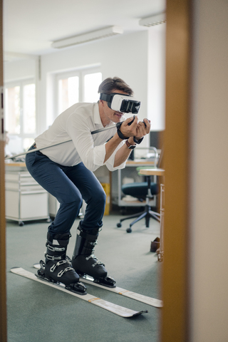 Geschäftsmann beim Skifahren im Büro, mit VR-Brille, lizenzfreies Stockfoto