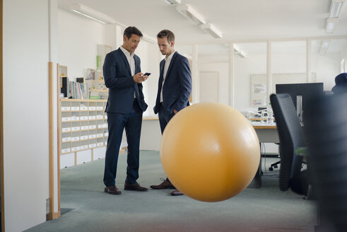 Zwei Geschäftsleute überprüfen ihr Smartphone mit einem gelben Fitnessball im Vordergrund - GUSF01194