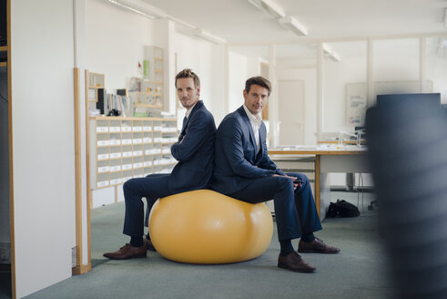 Zwei Geschäftsleute überprüfen ihr Smartphone mit einem gelben Fitnessball im Vordergrund - GUSF01196