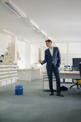 Businessman in office looking at wastepaper basket - GUSF01201