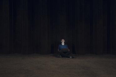 Mid adult man sitting cross-legged on ground, using laptop at night - GUSF01212