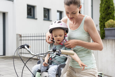 Mother and daughter, daughter wearing helmet sitting in children's seat - DIGF04953