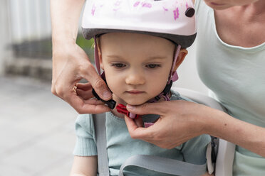 Mother and daughter, daughter wearing helmet sitting in children's seat - DIGF04956