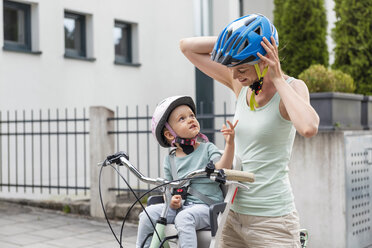 Mother and daughter wearing helmet, daughter sitting in children's seat - DIGF04957