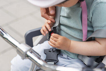 Mother and daughter, daughter sitting in children's seat and fastening seat belt - DIGF04958