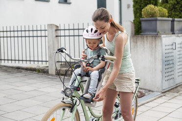 Mutter und Tochter fahren Fahrrad, die Tochter trägt einen Helm und sitzt auf dem Kindersitz - DIGF04960