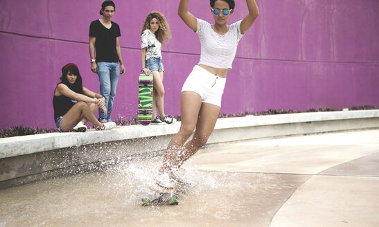 Eine junge Frau fährt auf einem Skateboard durch das Wasser. - MINF08576