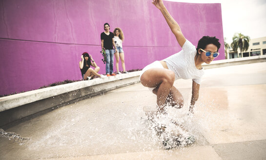 Eine junge Frau hockt sich auf ein Skateboard, um einen Wasserstrahl zu erzeugen. - MINF08578