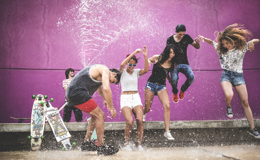 Eine Gruppe junger Menschen springt, während sie mit Wasser bespritzt werden. - MINF08584