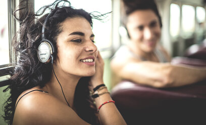 Two young people sitting on a bus wearing headphones. - MINF08599