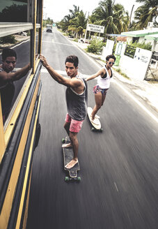 Zwei junge Leute fahren Skateboard und halten sich an einem fahrenden Schulbus fest. - MINF08602