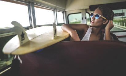 Junge Frau sitzt mit einem Surfbrett in einem Bus. - MINF08605