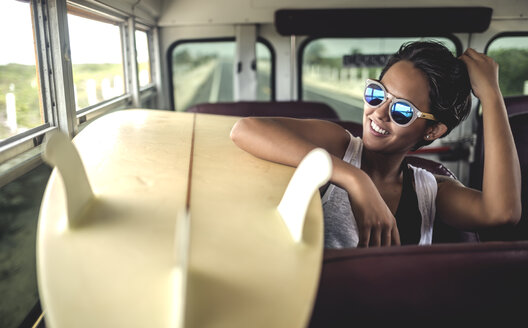 Junge Frau sitzt mit einem Surfbrett in einem Bus. - MINF08606