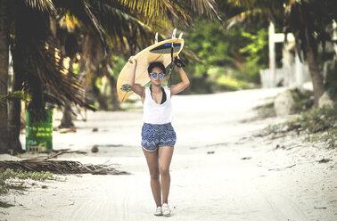 Junge Frau geht mit einem Surfbrett am Strand entlang. - MINF08607