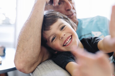 Nahaufnahme eines lächelnden Jungen mit braunem Haar und eines Mannes, der auf einem Sofa sitzt. - MINF08617