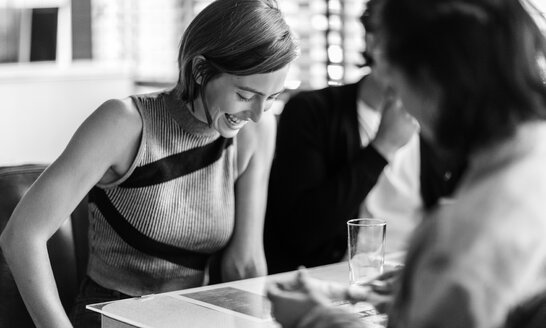 Lächelnde Frau, die mit zwei Freunden an einem Tisch in einem Diner sitzt und nach unten schaut. - MINF08618