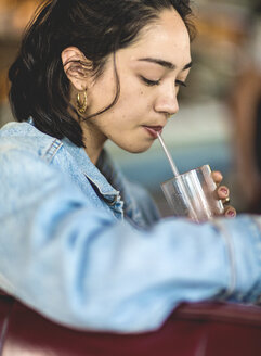 Young woman sitting at a bar counter, holding a glass, drinking with a straw. - MINF08621