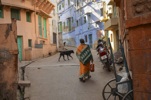 Urban street in Rajasthan, India, rear view of woman and dog walking. - MINF08635