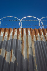 Low angle view of worn corrugated metal fence, razor wire above. - MINF08682