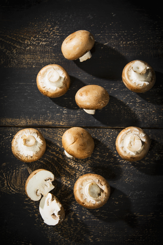 Geschnittene und ganze Crimini-Pilze auf dunklem Holz, lizenzfreies Stockfoto