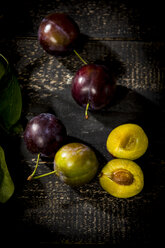 Whole and sliced plums on dark wood - MAEF12707