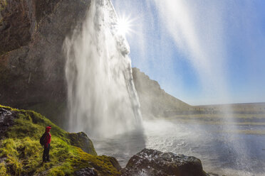 Eine Person steht am Rande eines Felsens in der Nähe eines Wasserfalls, der über eine steile Klippe stürzt. - MINF08734