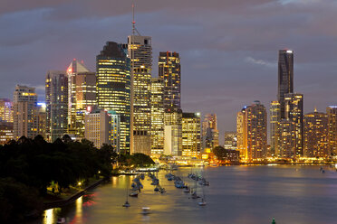 Skyline of city by the ocean at dusk, with illuminated skyscrapers, sailing boats moored near promenade. - MINF08749