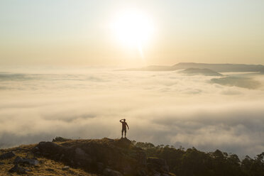 Rear view of man standing on top of mountain, admiring landscape view across misty valley. - MINF08753