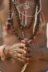 Nahaufnahme eines hemdlosen Mannes mit Körperbemalung, der Perlenketten trägt und die Hände zum Gebet verschränkt. - MINF08811